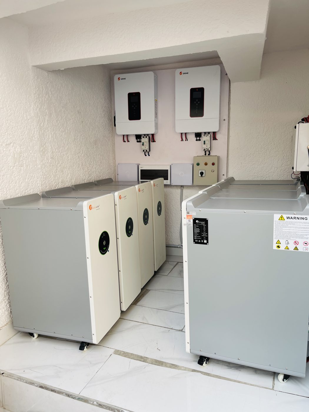 Two solar inverters on a wall above large battery packs on wheels